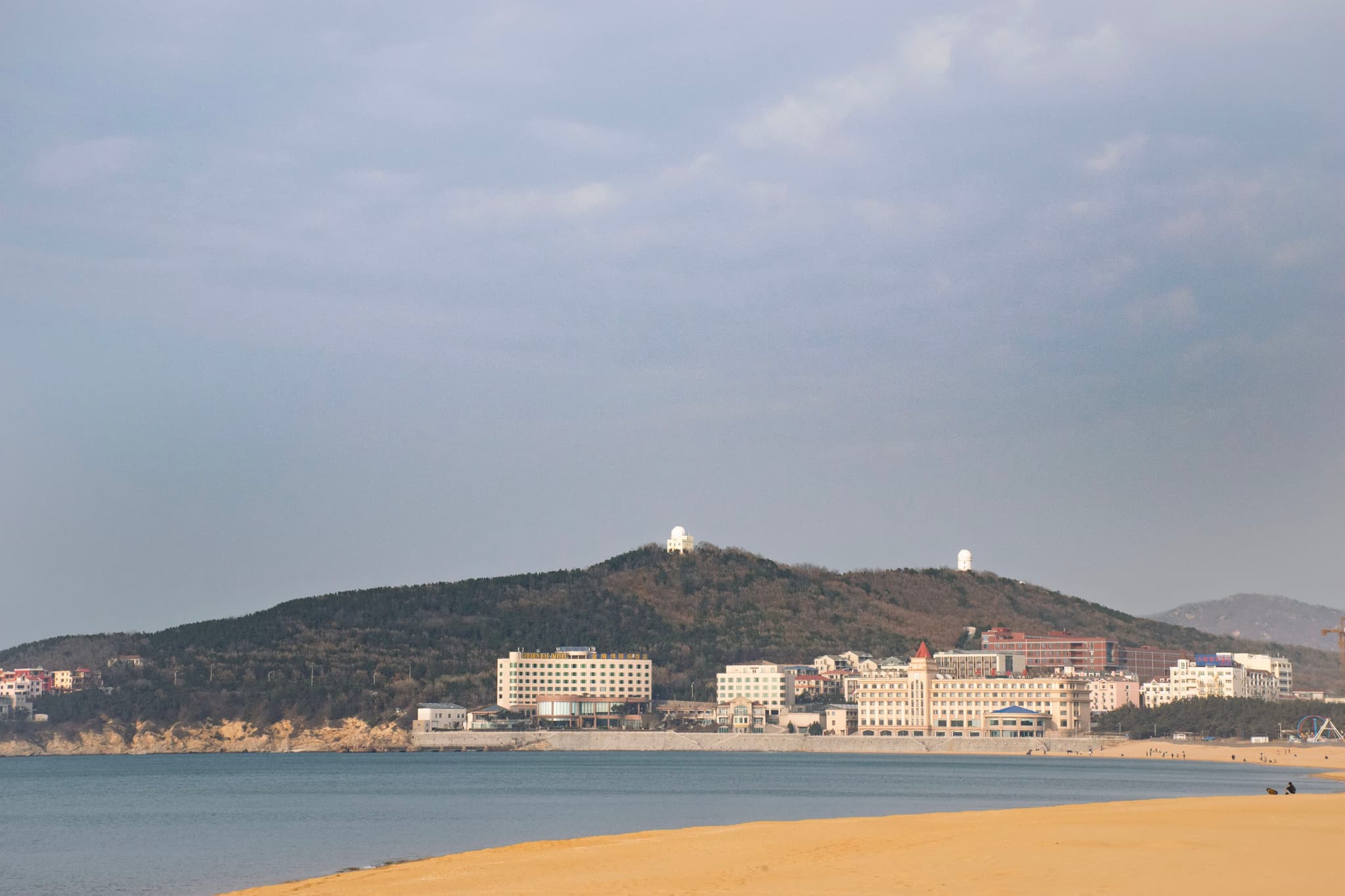 海滩前方是蓝色的海水，背景是山丘和建筑物。