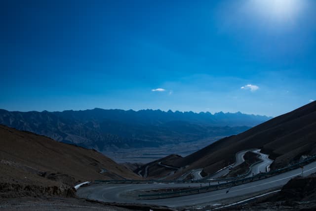 蜿蜒的山路在高山间穿行，远方是连绵的山脉和湛蓝的天空。