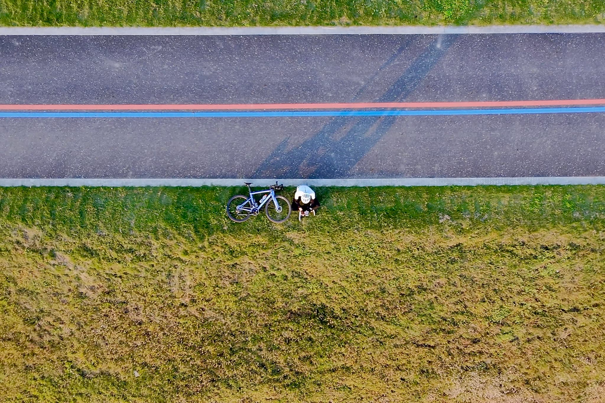 一条笔直的公路旁边，一个人坐在草地上，旁边停放着一辆自行车。