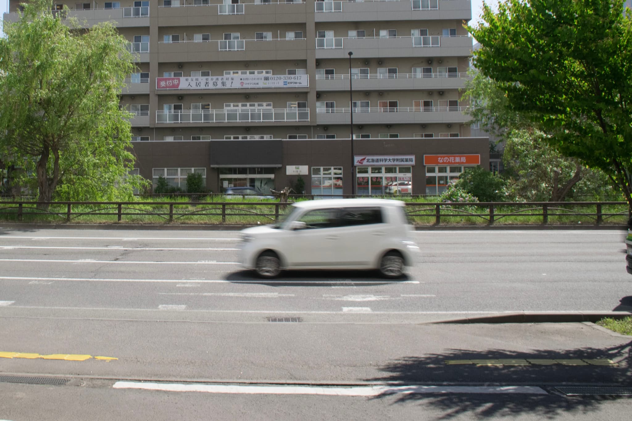 白色汽车在道路上行驶，背景是多层建筑和绿树。