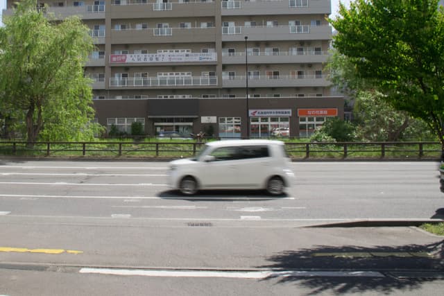 白色汽车在道路上行驶，背景是多层建筑和绿树。