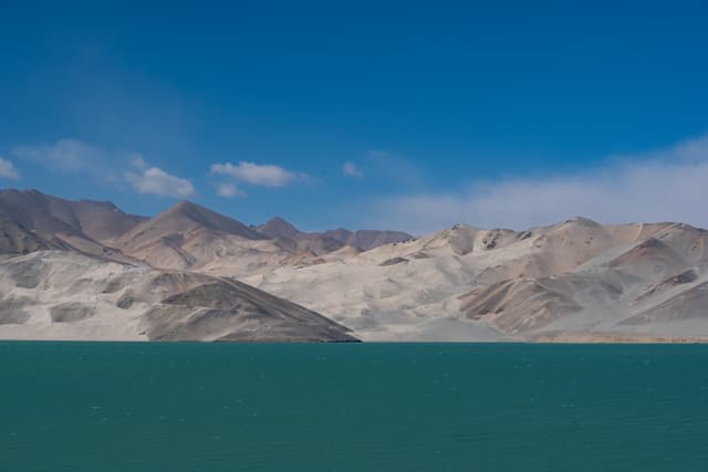 蓝天下的山脉和湖泊，湖水呈深绿色，山脉覆盖着少量积雪。