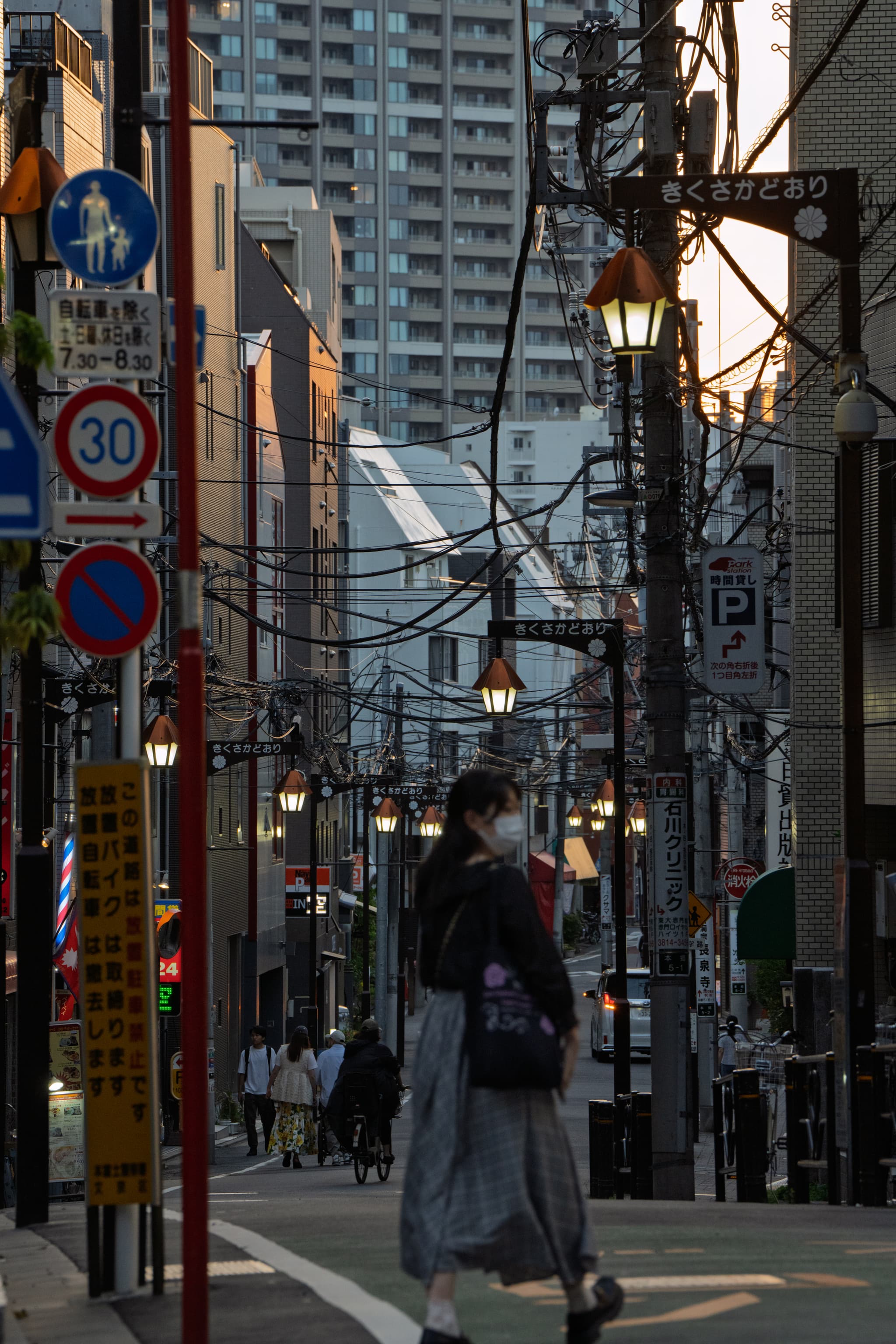 城市街道，路灯和电线交错，高楼林立，行人走在人行道上。