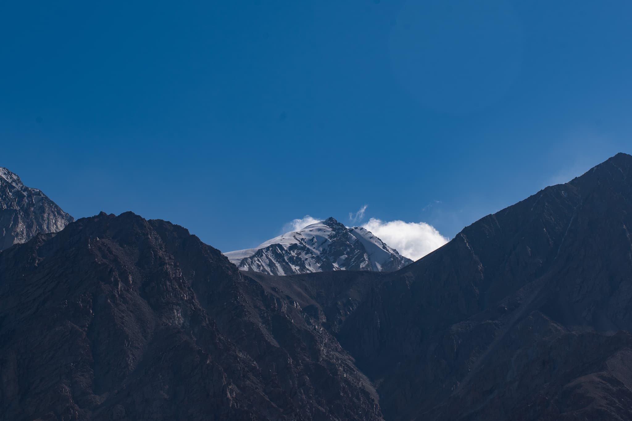 雪山在蓝天映衬下，山峰间有少量云雾。