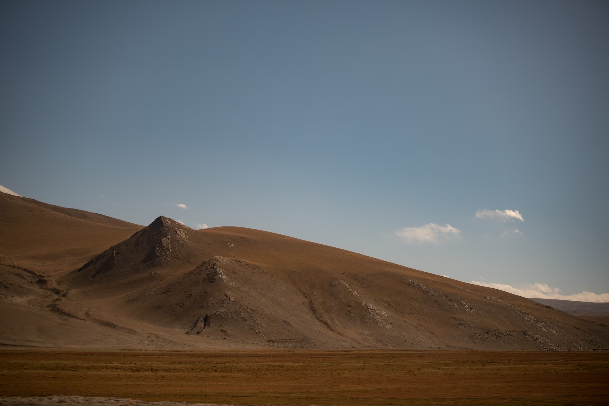 荒凉的山坡和广阔的平原，背景是晴朗的蓝天。