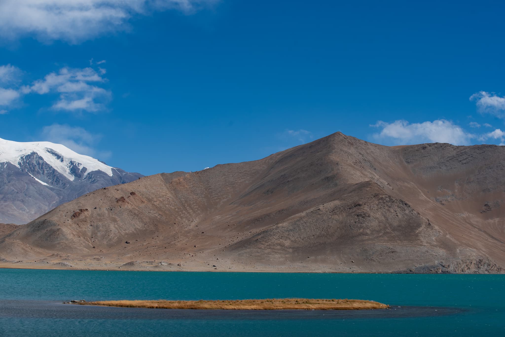 雪山和湖泊，湖中有一小岛，蓝天白云。