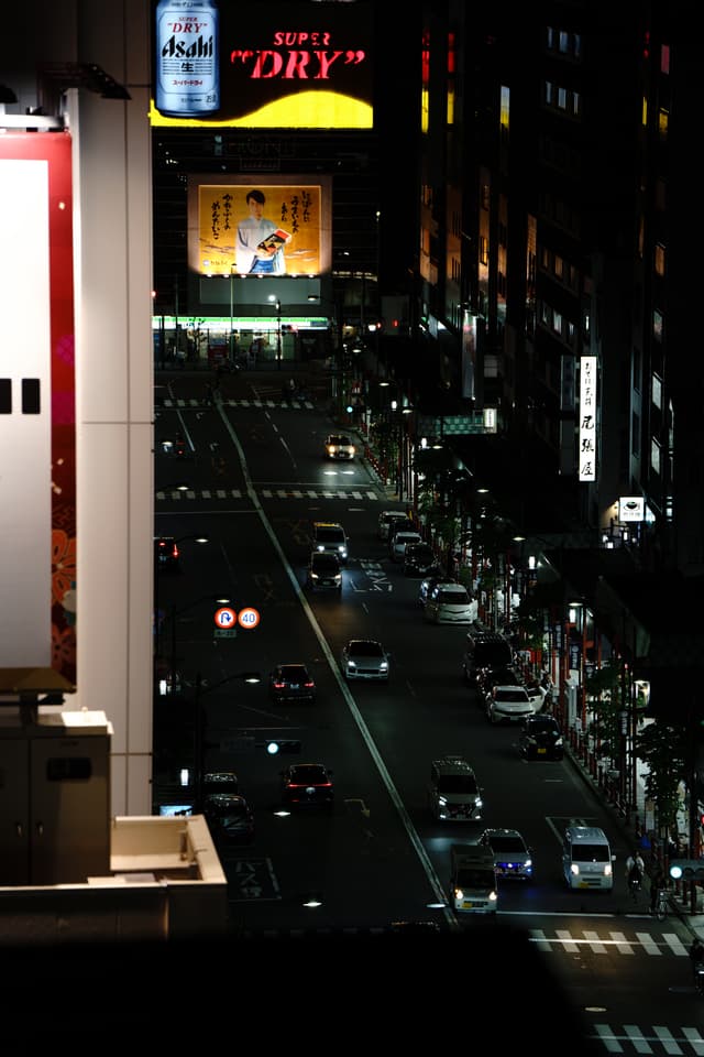 夜晚的城市街道，车辆行驶在灯光照亮的道路上，远处有一个大型广告牌。