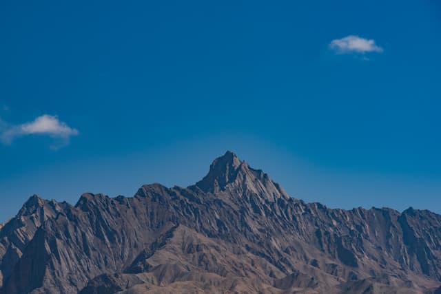 高耸的山峰在湛蓝的天空下，山顶有几朵白云。