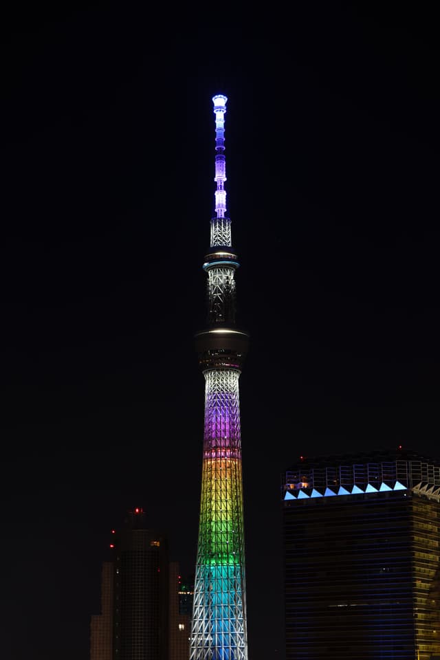 夜空中，一座高塔被彩虹色灯光照亮，周围有几座建筑物。