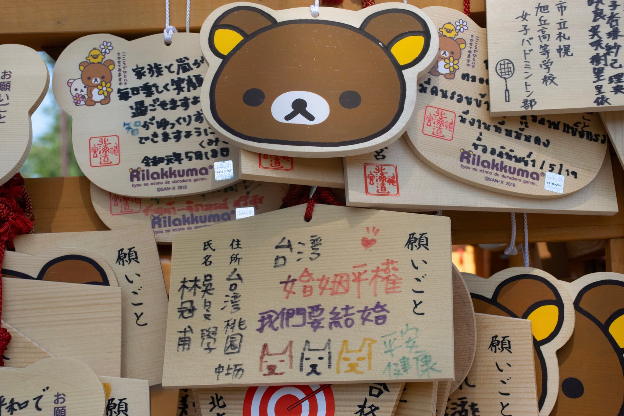 木牌上挂着卡通熊猫图案和日文书写，背景有更多类似的木牌。