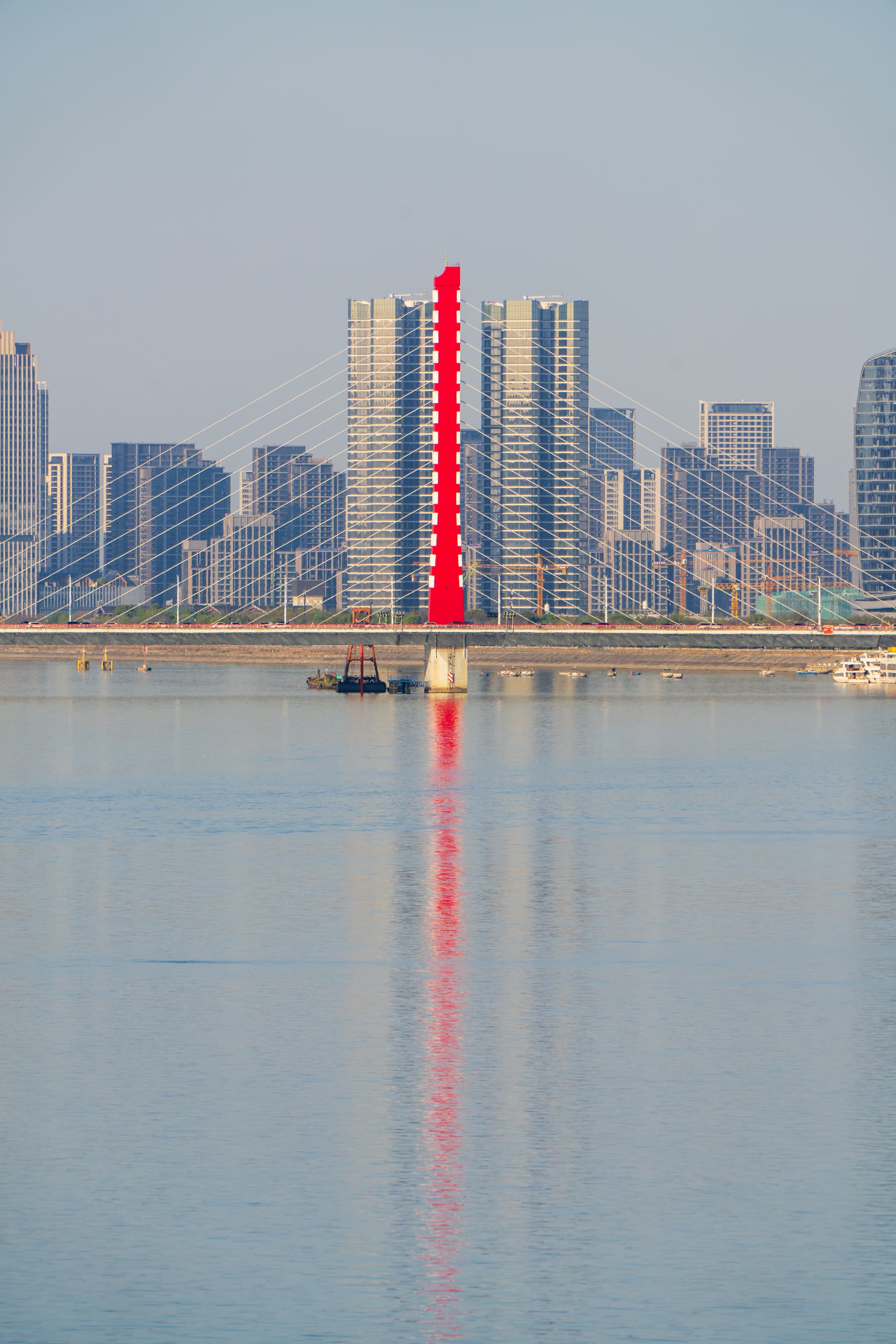 一座红色桥梁横跨水面，背景是现代城市天际线，桥梁在水中形成倒影。