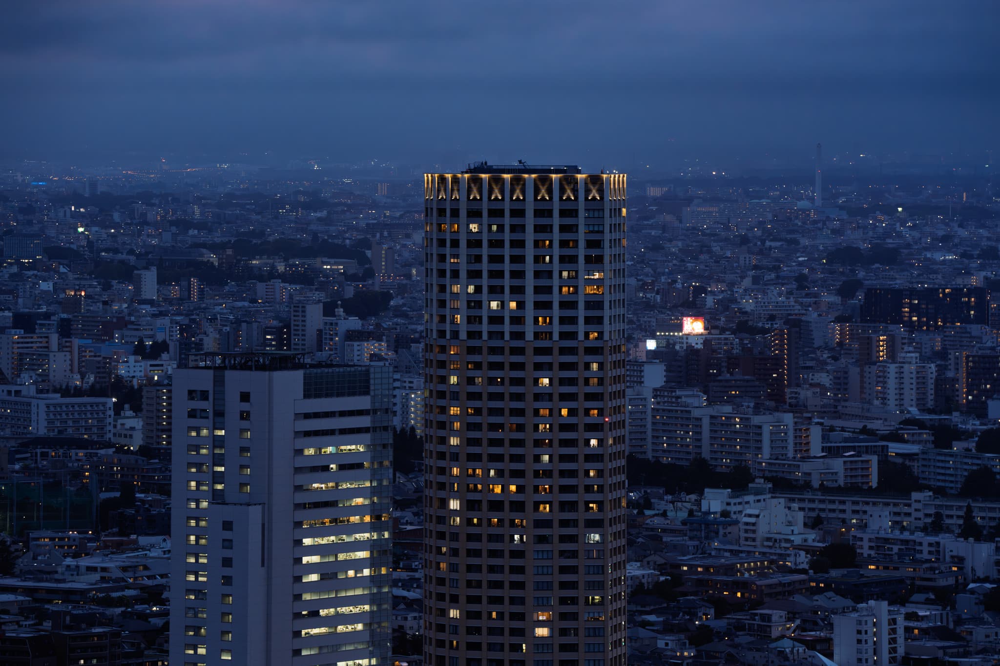 夜幕降临的城市景观，高楼大厦灯火通明，远处的建筑在昏暗的天色中隐约可见。