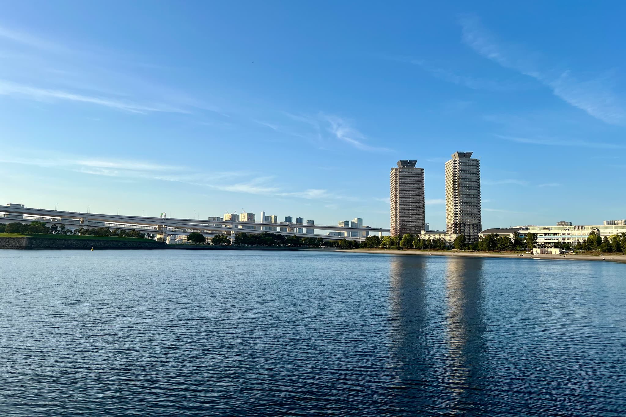 湖面平静，远处有两座高楼和一座桥，蓝天白云映衬着城市景观。