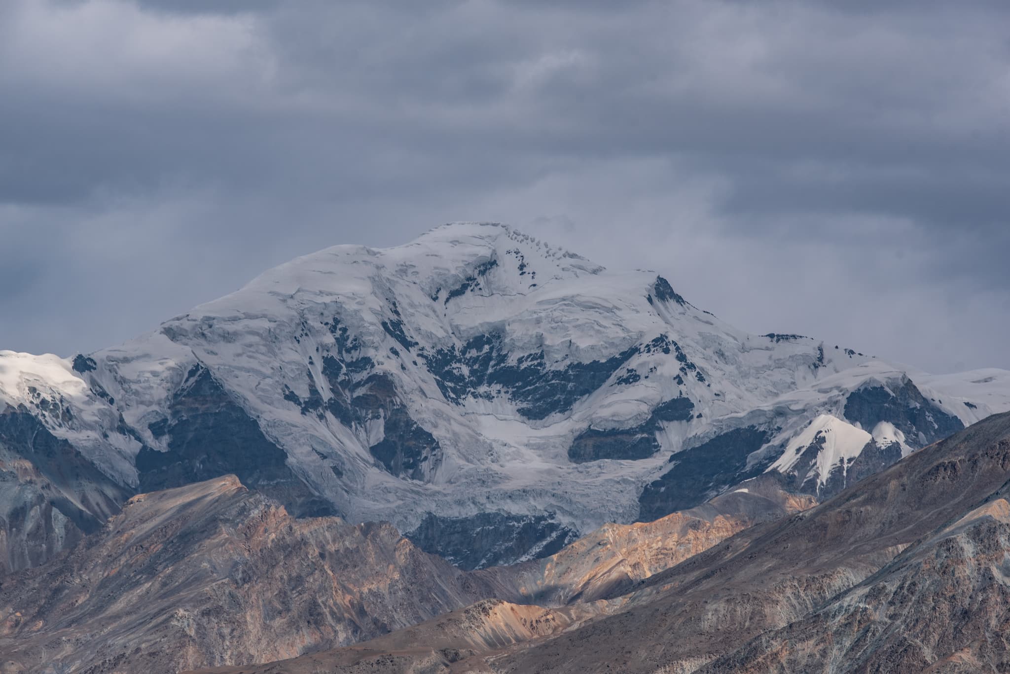 雪山在云层下若隐若现，山麓覆盖着积雪，山脚下是起伏的山峦。